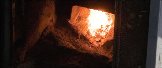 A wood pellet boiler with door open to show burning